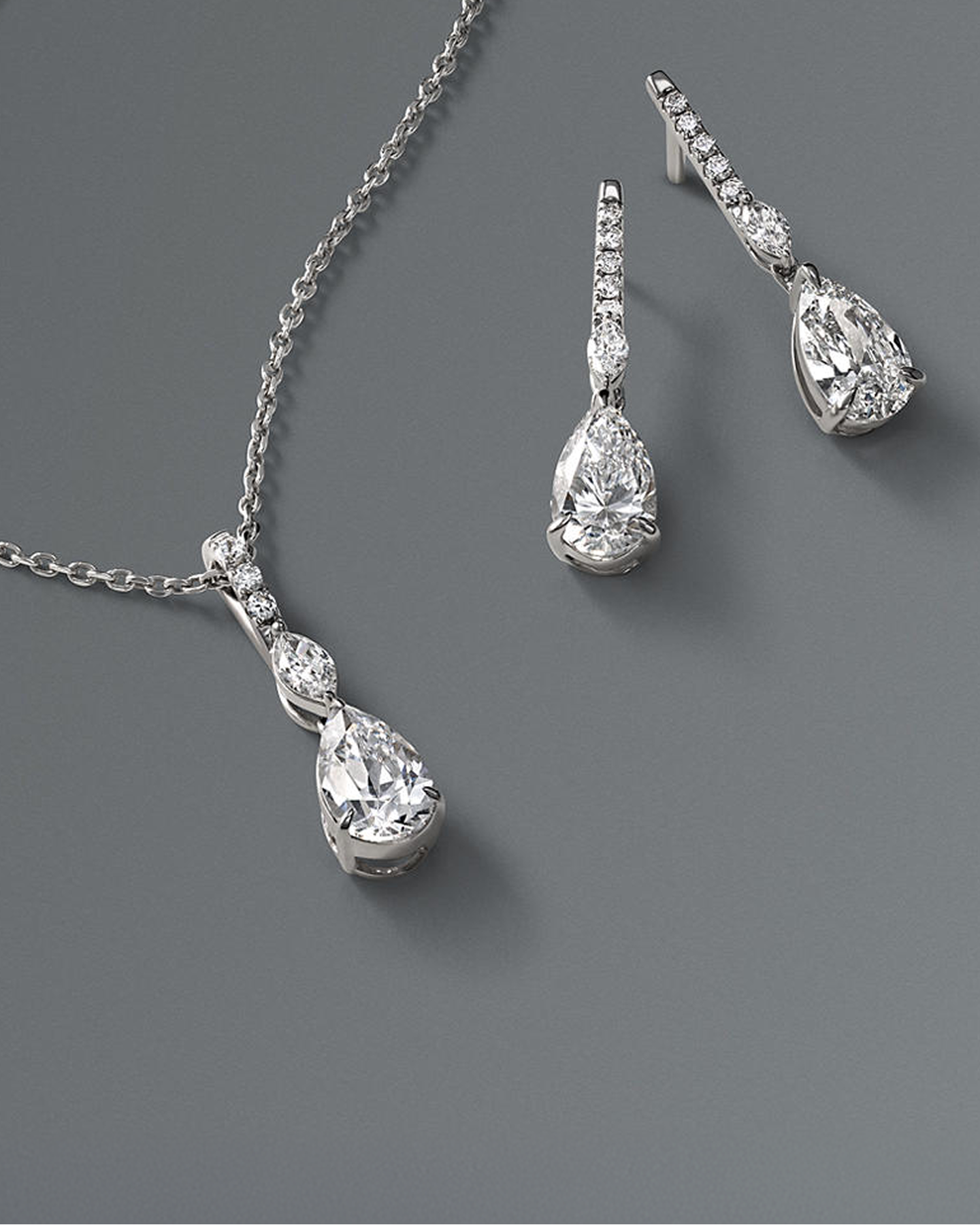 Kay diamond pear-shaped pendant necklace and matching drop earrings featuring brilliant pear-cut and marquise-cut diamonds set in white gold, showcased in an elegant fine jewelry flat lay on a soft gray background.