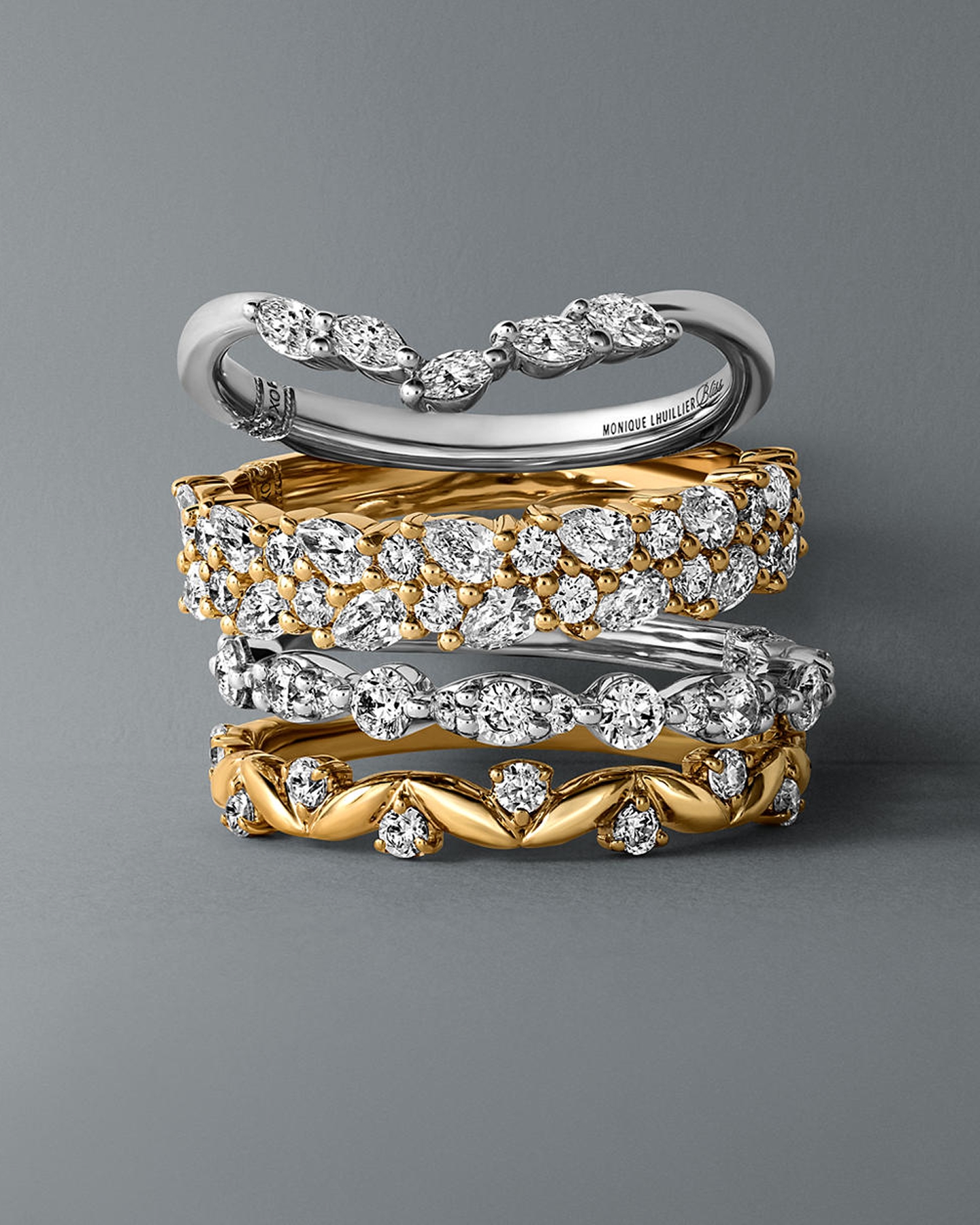 Kay diamond wedding band stack featuring mixed metal yellow gold and white gold bands adorned with round, marquise, and pear-shaped diamonds, showcasing elegant bridal ring designs from the Uniquely Bliss collection on a soft gray background.
