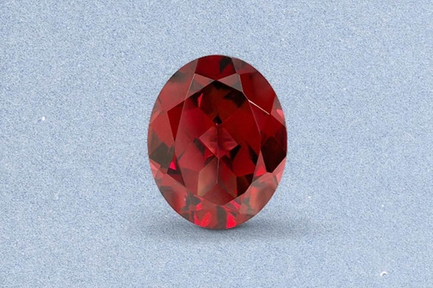 Kay oval-cut garnet gemstone featuring deep red color, brilliant faceting, and rich sparkle on a light neutral background