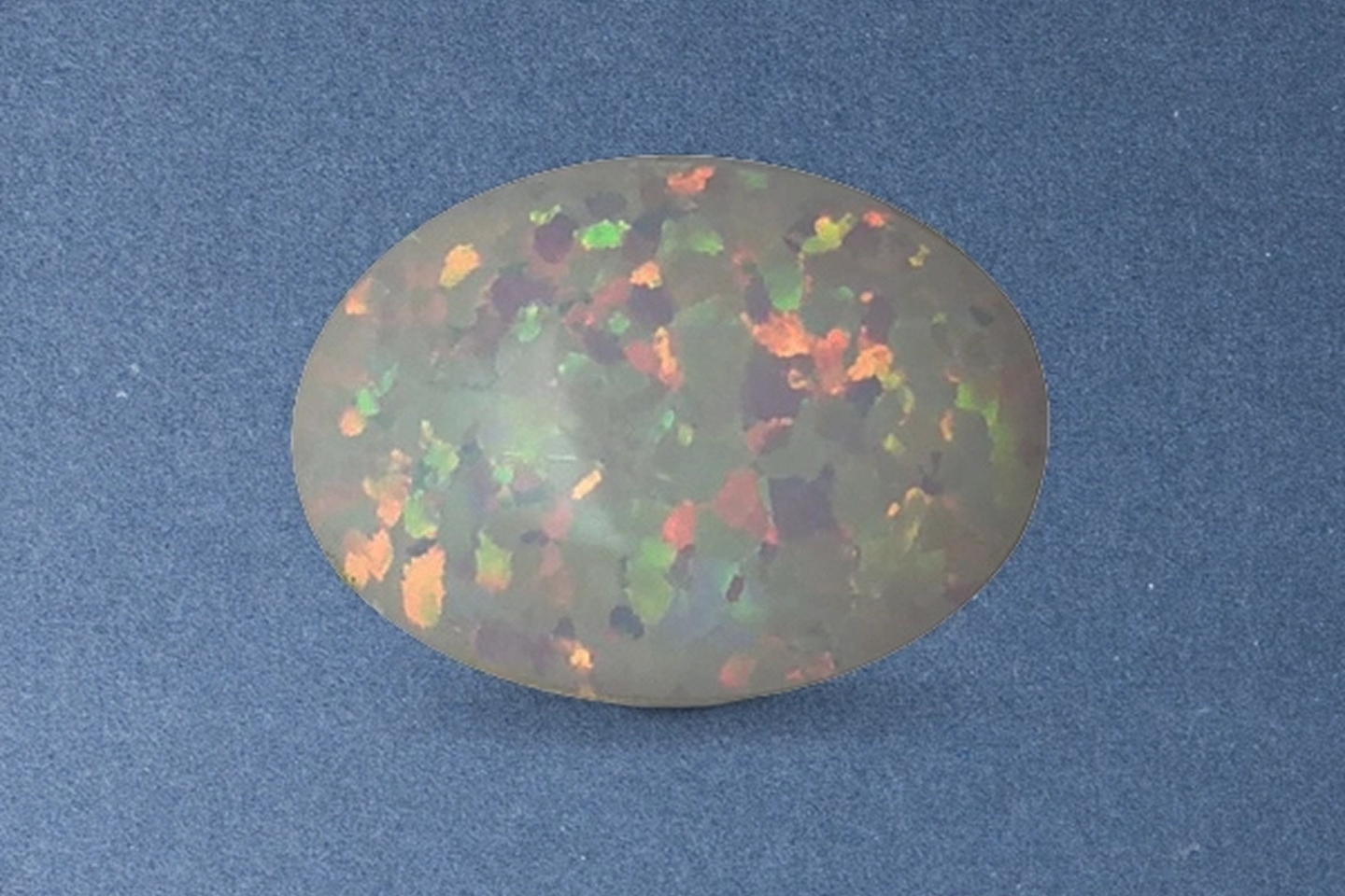 Kay oval black opal gemstone featuring vibrant flashes of green, red, and orange play-of-color on a dark body tone
