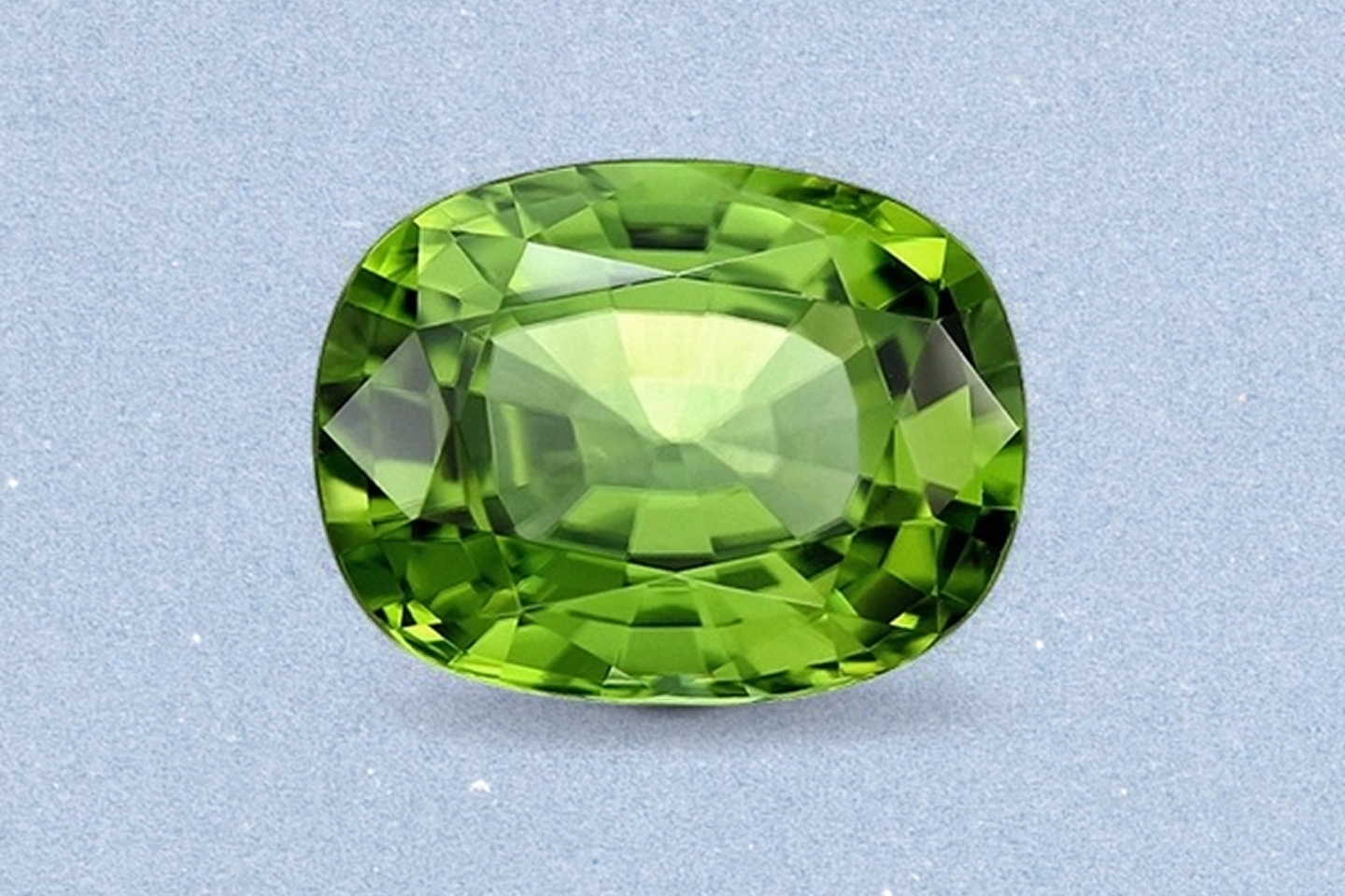 Kay cushion-cut peridot gemstone featuring vibrant lime-green color, brilliant faceting, and exceptional clarity on a light neutral background