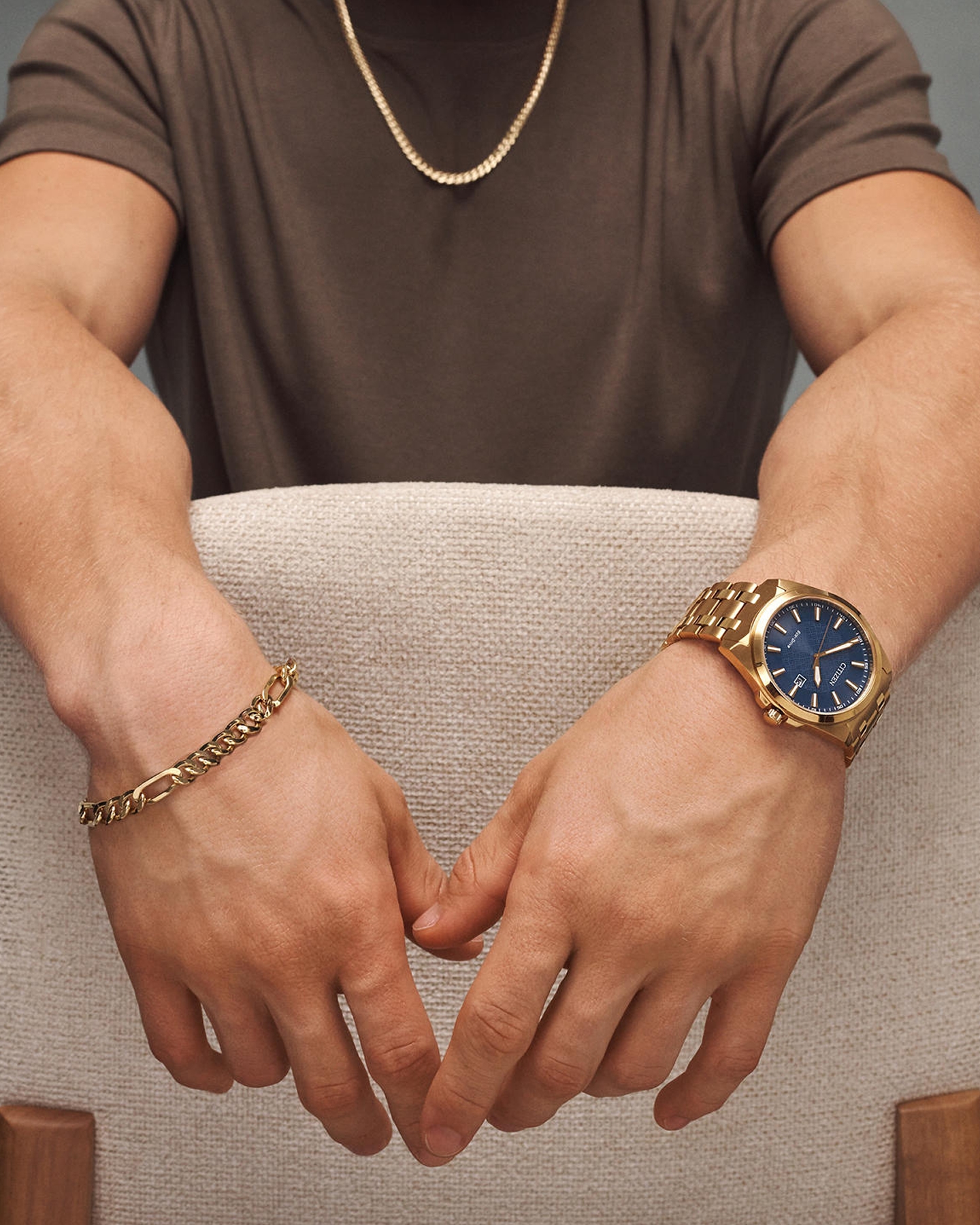 Kay men's gold jewelry featuring a curb chain necklace, matching bracelet, and gold-tone blue dial watch styled in a modern lifestyle setting