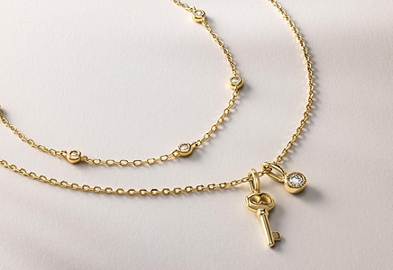 Two gold necklaces. One with diamond studs, and another with a key pendant and a diamond pendant attached from KAY.