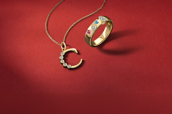 A gold necklace with a gold, diamond studded "C," and a gold ring with various gemstones, from KAY.