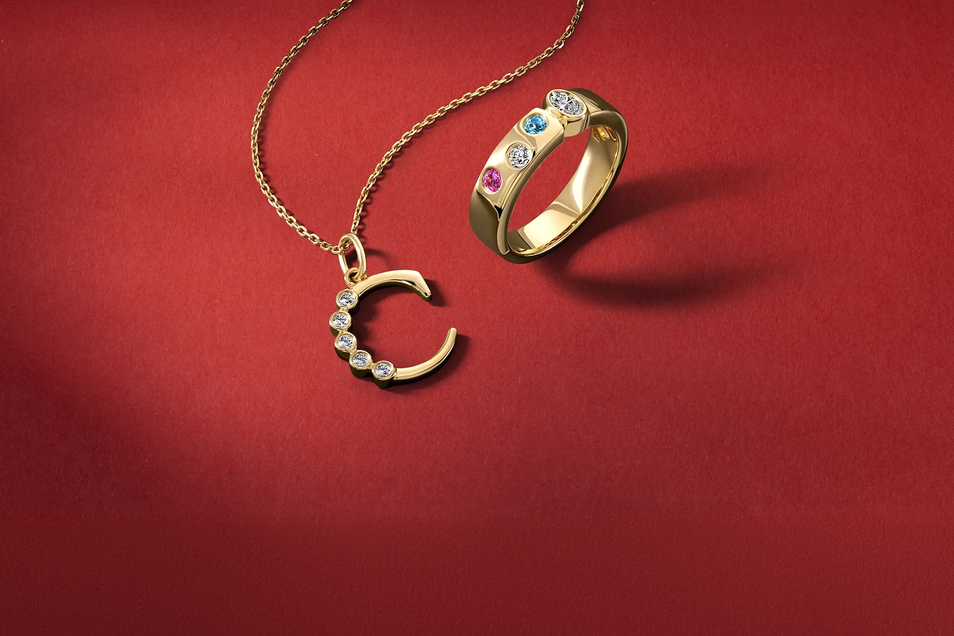 A gold necklace with a gold, diamond studded "C," and a gold ring with various gemstones, from KAY.