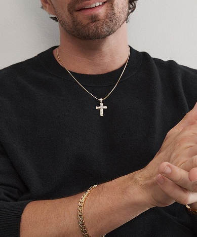 A man wearing a gold chain with a gold cross, and a gold chain bracelet from KAY.