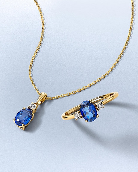 A gold chain necklaces with a royal blue sapphire and diamond pendant, and matching gold ring by KAY.