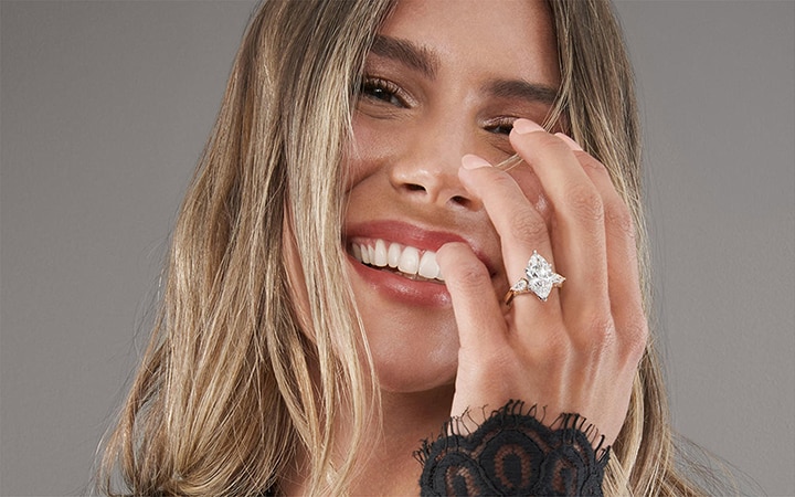 A woman wearing a gold band engagement ring with a marquise cut diamond, by KAY.