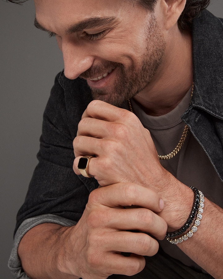 A man wearing a stylish gold and black diamond ring, with a gold cuban chain necklaces from KAY.