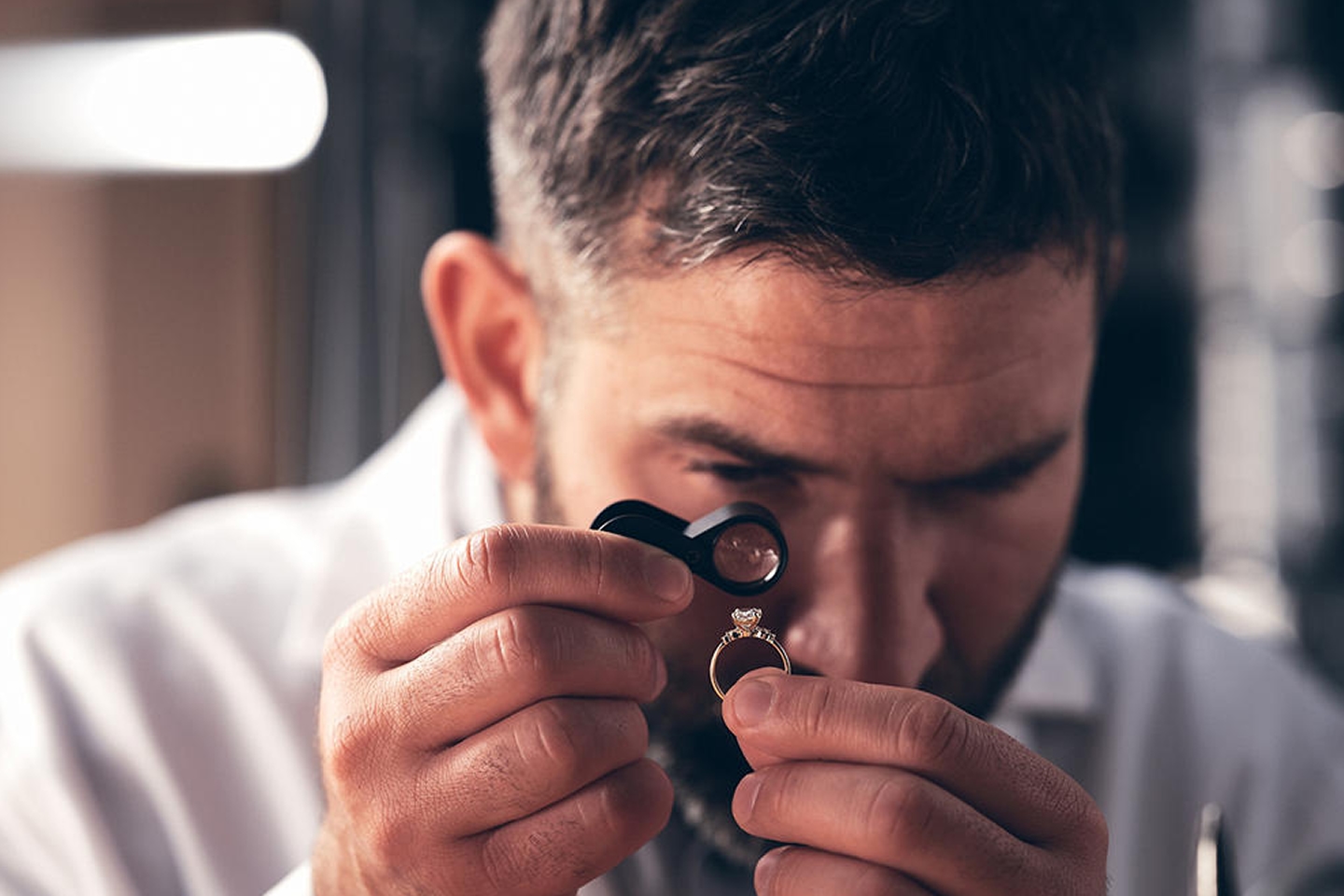 A jewelry technician closely examining the diamond of an engagement ring from KAY.