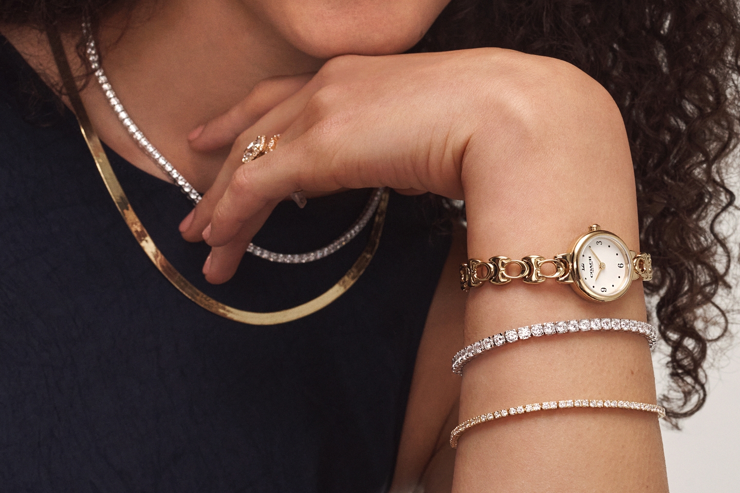 A woman sporting a pearl necklace, a gold herringbone necklace, and various wrist apparel from KAY.