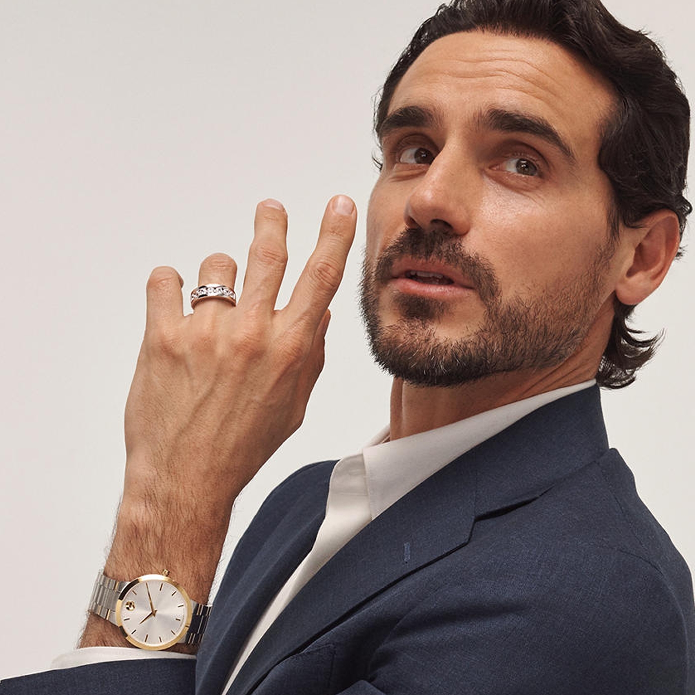 A groom in a blue suit showing off his white gold diamond engagement ring and stainless steel watch from KAY.