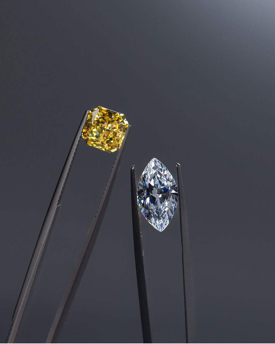 Two different colored diamonds, one with a yellow tint and the other more clear, helpd by tweezers.