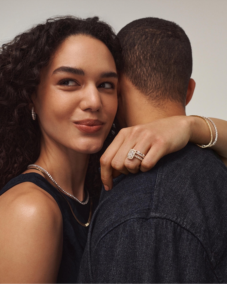 A couple embracing each other in a hug. The woman is wearing diamond bracelets, necklaces, earrings, and a ring from KAY.