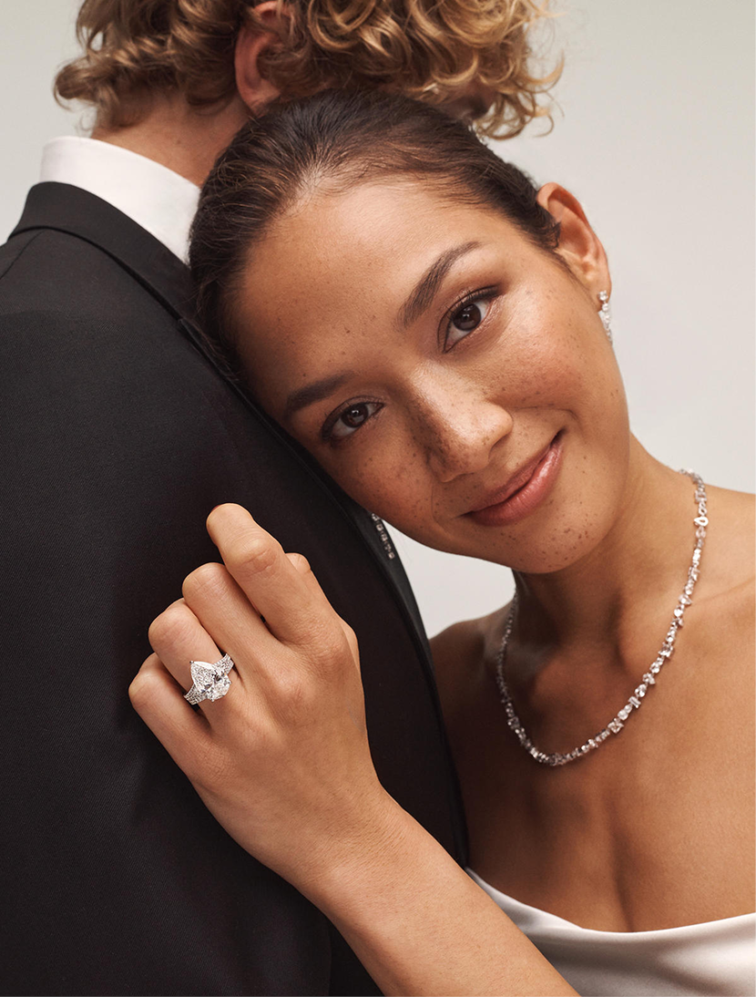 A bride hugging the groom while wearing a diamond ring with a matching diamond necklace from the Neil Lane Artistry Collection.