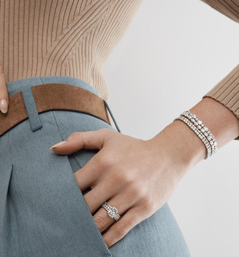 A woman holding her belt, wearing a trio of diamond bracelets from KAY.