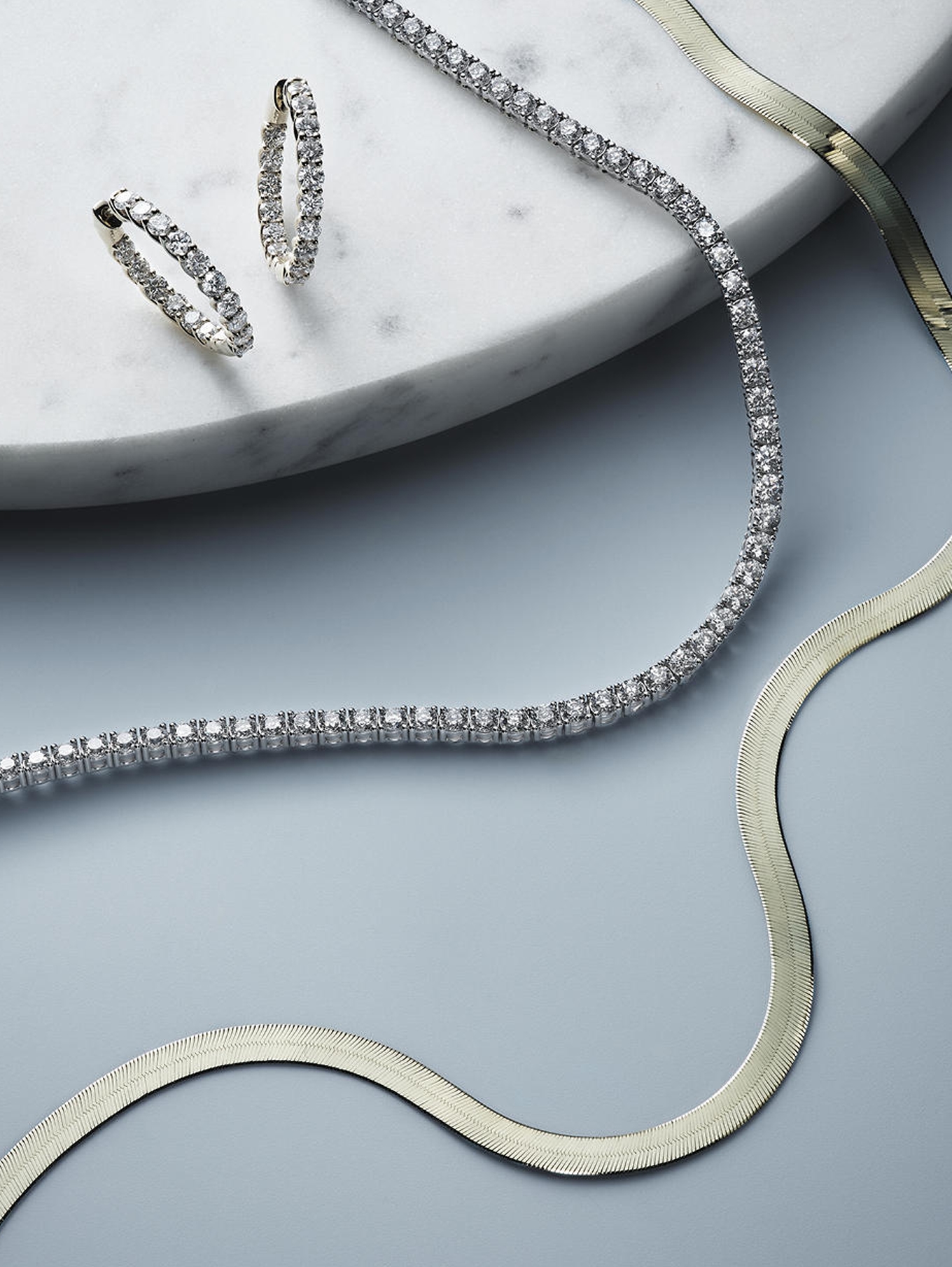 A set of diamond tennis earrings, a matching diamond tennis necklaces, and a gold herringbone necklace from KAY.