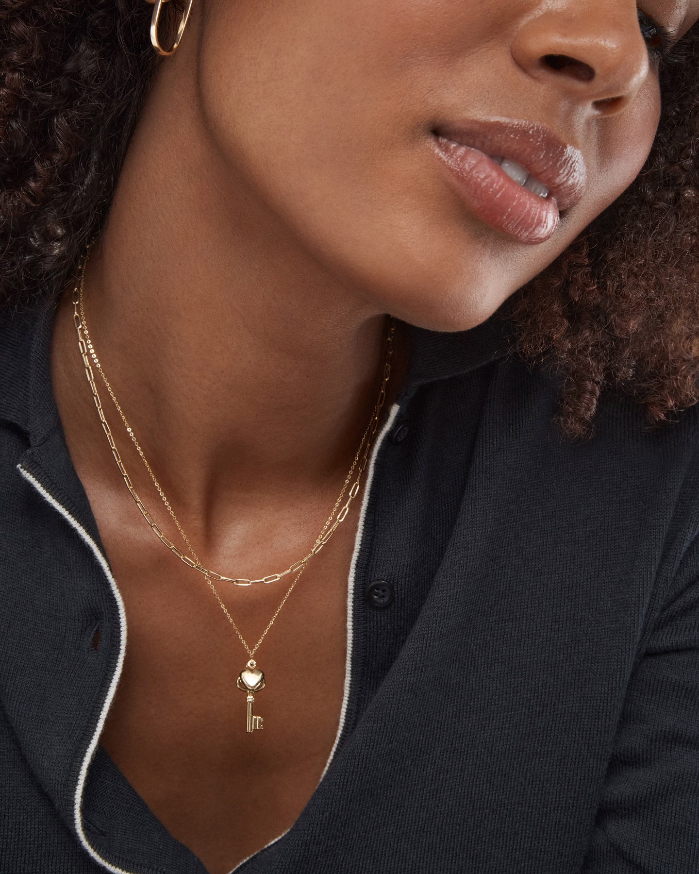 A woman sporting two gold necklaces, one with a key pendant.