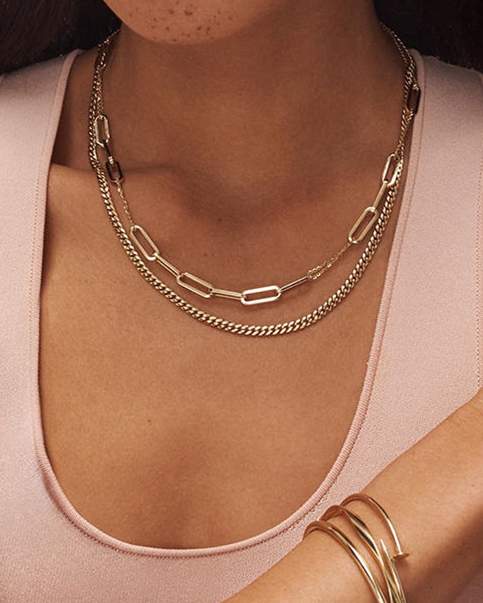 A model wearing a gold chain link necklace and a gold figaro chain necklace from KAY.