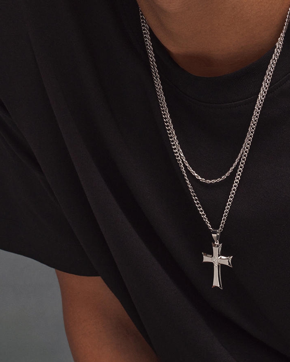 a man wearing two silver and stainless steel layering necklaces, one with a cross pendant from KAY.