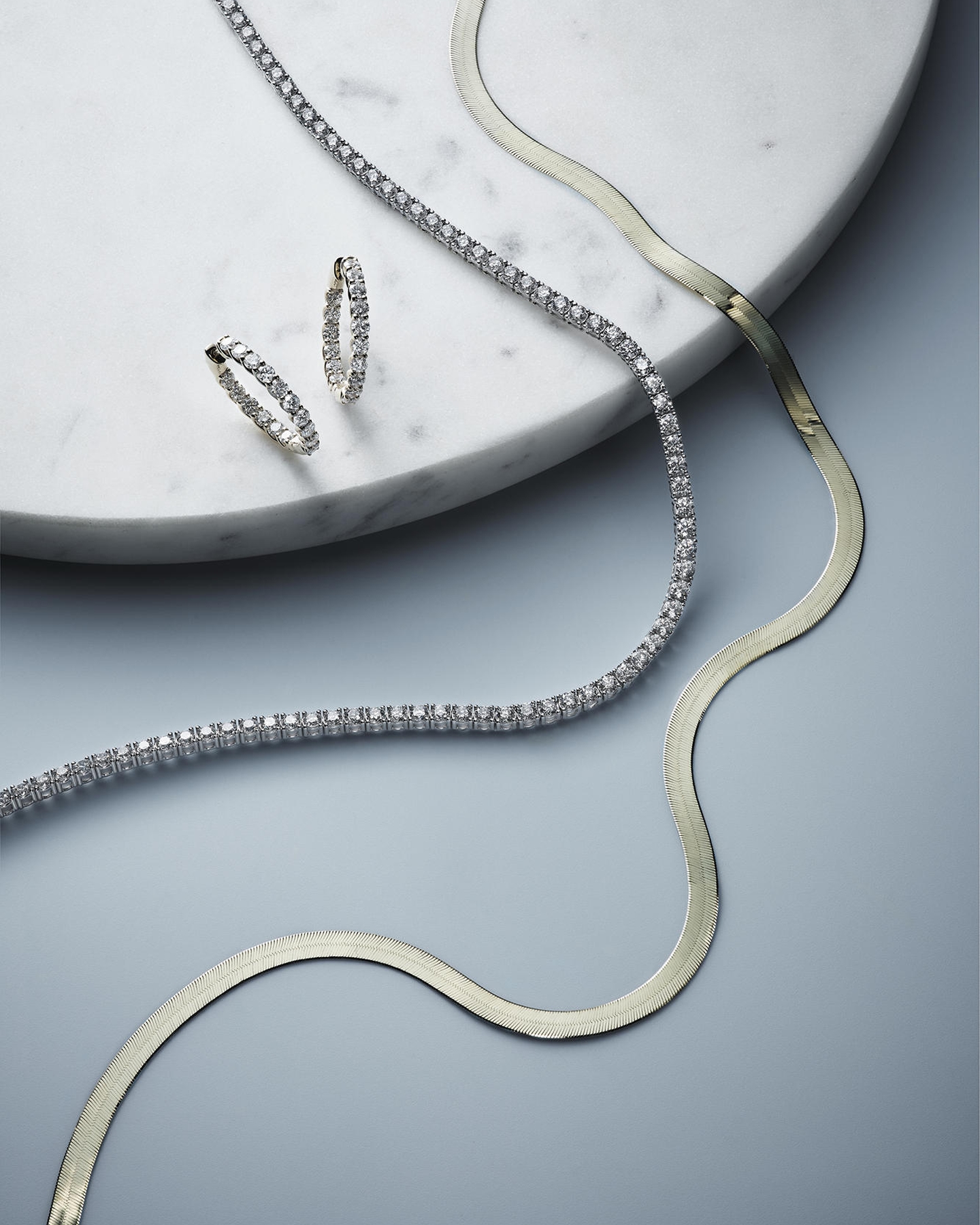 New Classics featuring a pair of diamond studded earrings, a tennic necklace, and a flat gold necklace from KAY.
