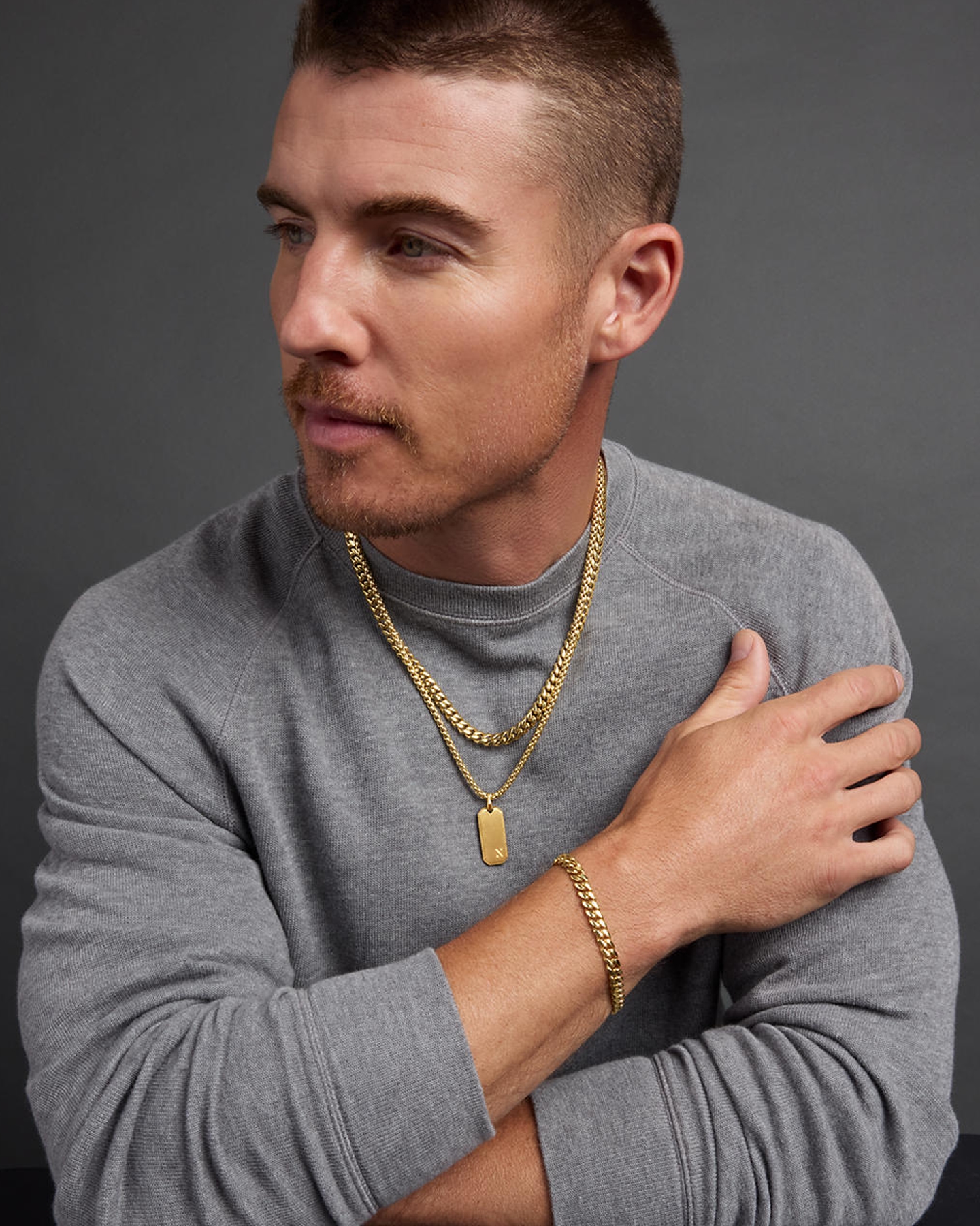 A man sporting a double gold chain with a gold pendant, and a gold chain bracelet by Jaxxon, from KAY.