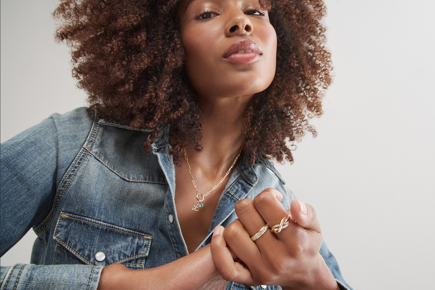 A woman wearing a denim jacket, showing off her silver necklace and rings from KAY.