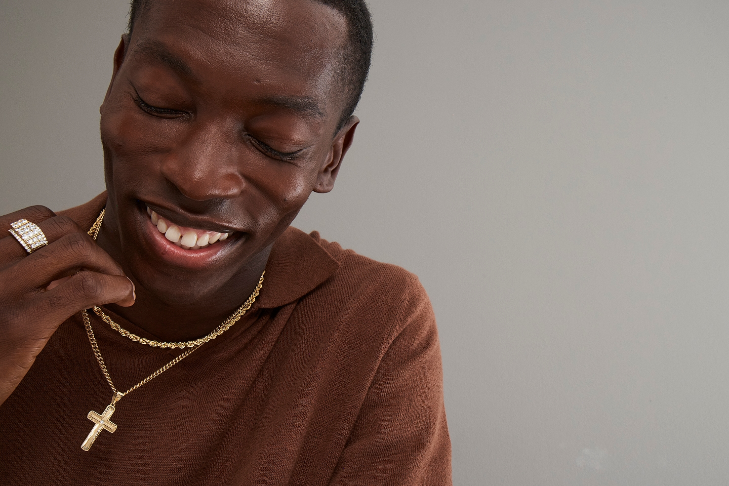 A man wearing a diamond ring, a gold chain, and a gold necklace with a cross pendant from KAY.