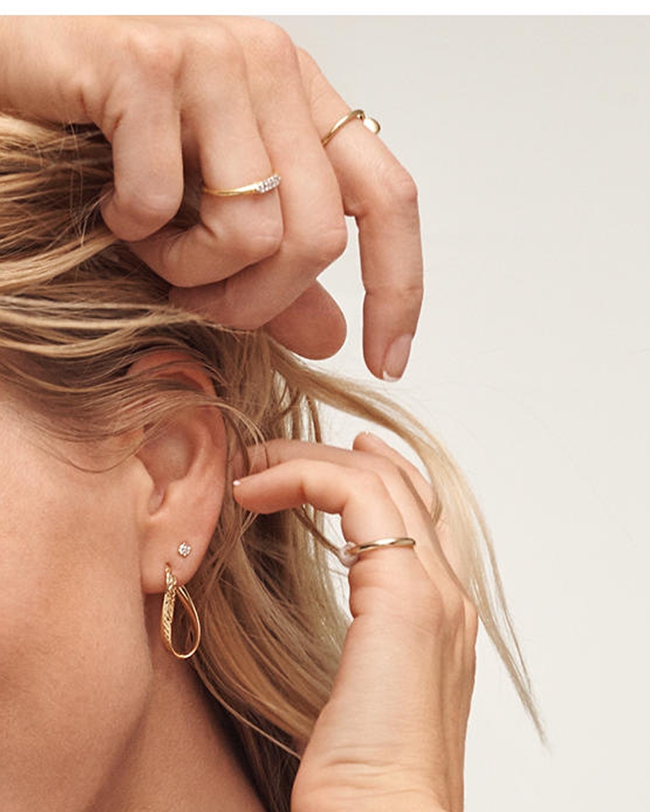 A woman wearing multiple gold rings to match her gold earring from KAY.