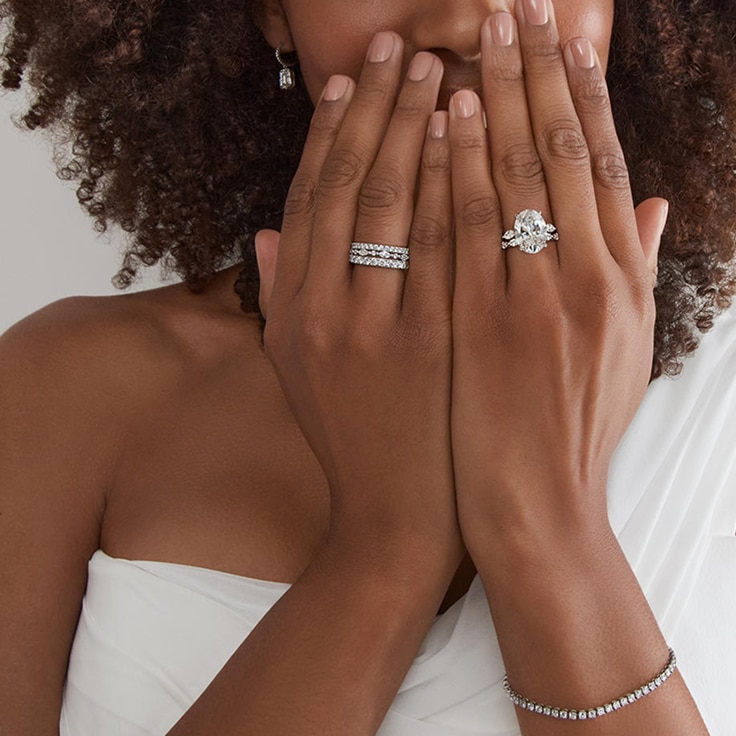 Woman wearing wedding dress, diamond engagement ring, other rings, earrings, and bracelet