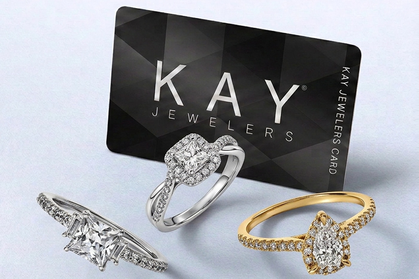 Kay Jewelers credit card behind three diamond engagement rings on light blue background