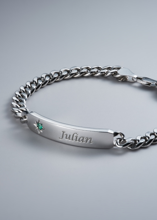 A silver personalized, name-engraved bracelet with an inlaid emerald.