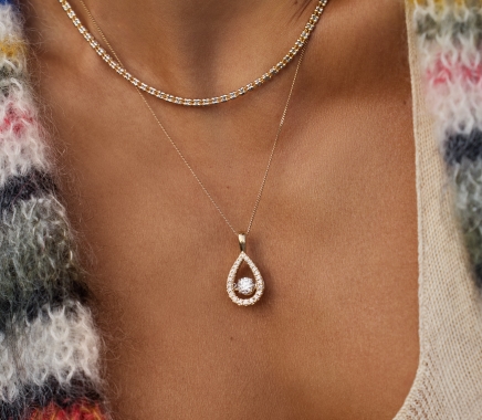 A woman wearing a gold tear-drop shaped pendant studded with diamonds.