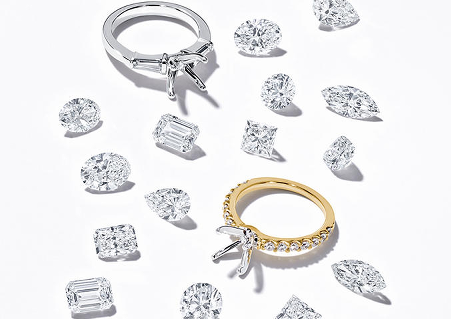 Kay engagement ring settings in white and yellow gold displayed alongside loose round, oval, pear, marquise, princess and emerald-cut diamonds, showcasing diamond shape options for creating a personalized engagement ring.