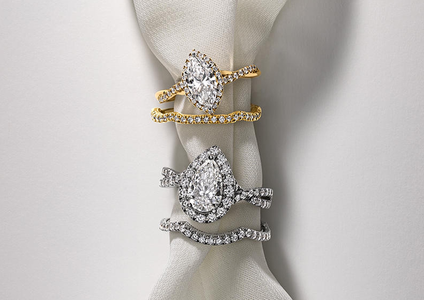 Kay diamond bridal ring sets featuring marquise-cut and pear-shaped diamond engagement rings with matching diamond wedding bands in yellow gold and white gold, displayed on elegant white fabric.