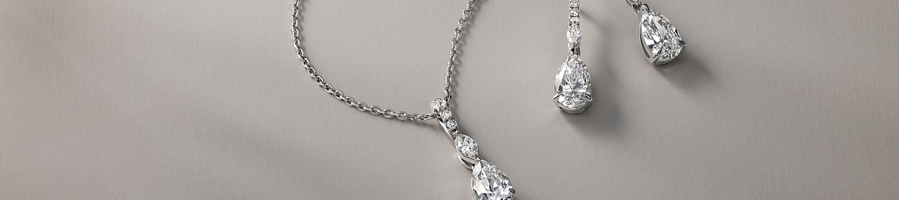 Monique Lhuillier Bliss pear diamond necklace and drop earrings on gray background