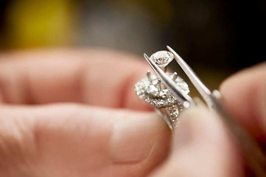 Image of hand placing diamond into a ring setting