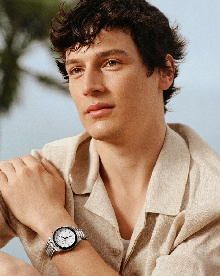 Man with dark hair wearing beige shirt and silver tone Tissot watch with palm tree in background