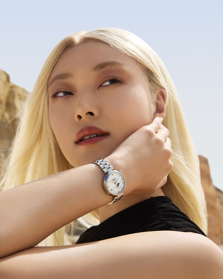 Woman with blonde hair wearing black top and moon phase Tissot watch with cliffs in background