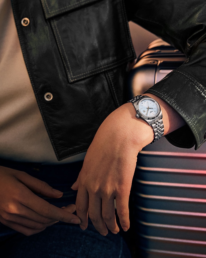Woman wearing Tissot watch resting arm on suitcase