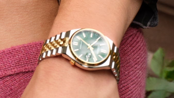 A man wearing a silver banded watch with an emerald face.