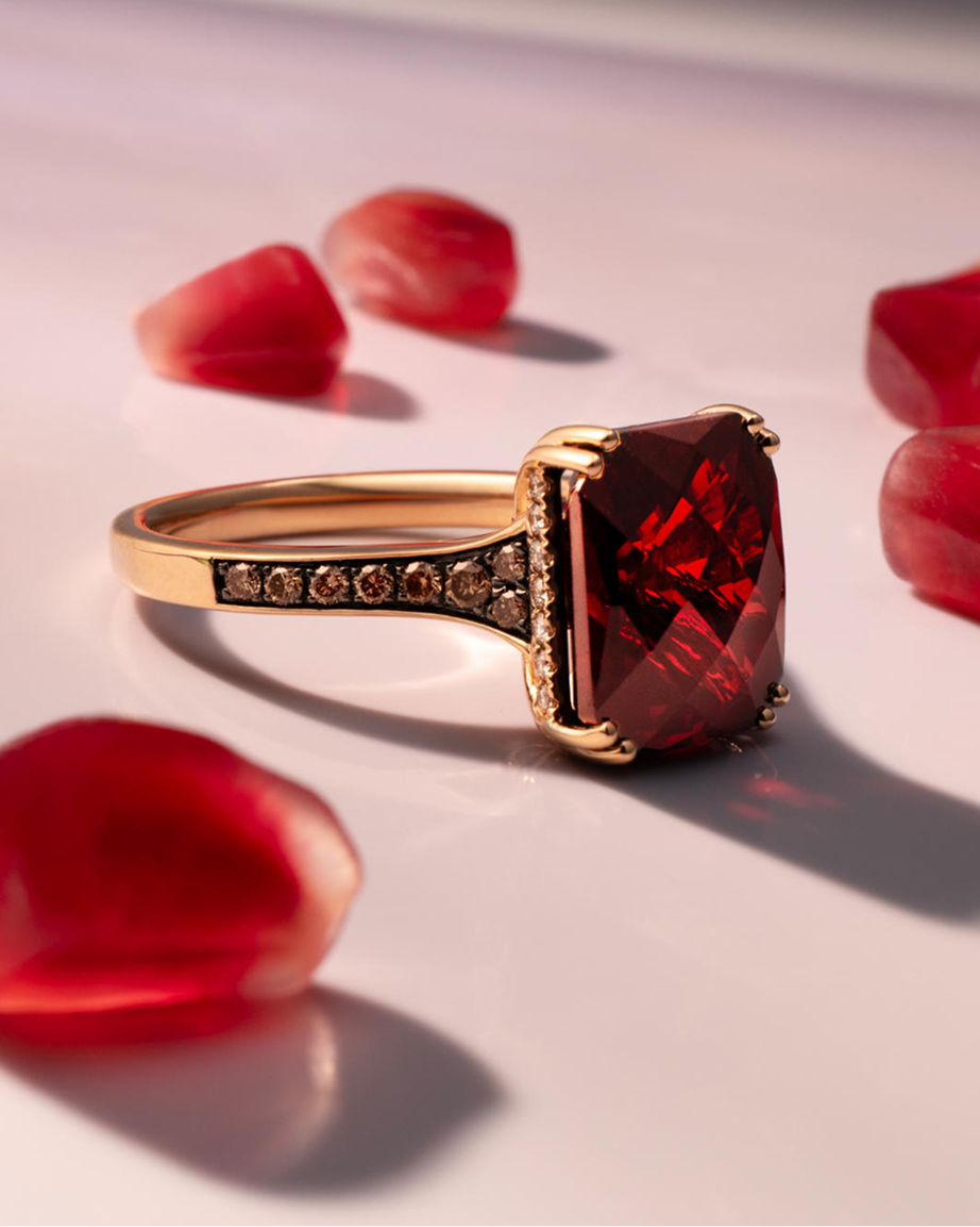 Cushion-cut deep red gemstone ring in yellow gold with diamond-accented details, artfully styled among vibrant red gemstone accents to showcase rich color, dramatic brilliance, and luxury fine jewelry craftsmanship for Kay.