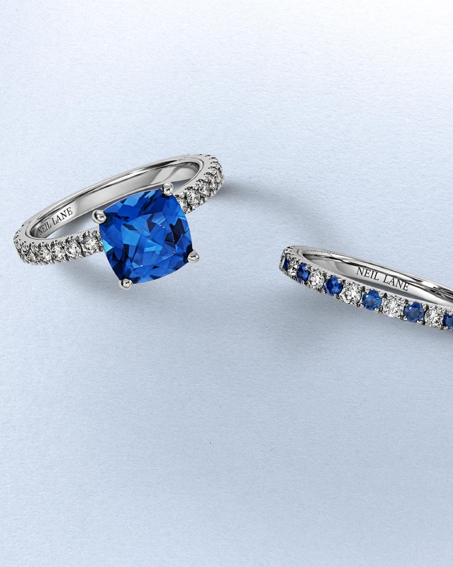 Kay Neil Lane gemstone engagement rings featuring a vivid cushion-cut blue sapphire ring and a coordinating sapphire and diamond band in white gold, showcasing vibrant color, diamond accents, and designer-inspired elegance.